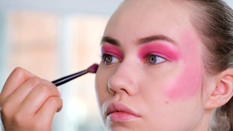 Unrecognizable-visagist-applying-fluid-foundation-on-young-woman's-face-using-sponge.-Professional-makeup-in-salon.-Nude-makeup