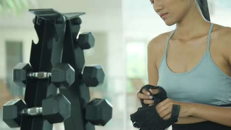 Attractive-asian-female-wearing-sports-clothes-putting-on-sports-gloves-before-workout-in-gym.-Young-woman-getting-ready-for-exercise