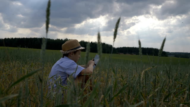 boy-sits-in-a-field-against-beautiful-clouds-and-uses-a-tablet-in-the-evening