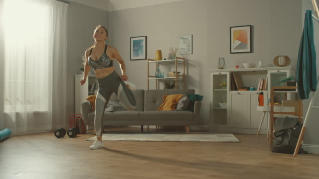 Beautiful-Busty-Athletic-Fitness-Girl-in-Sportswear-is-Doing-Cardio-Exercises-in-Her-Sunny-and-Spacious-Apartment-with-Minimalistic-Interior.