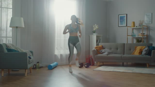 Strong-and-Beautiful-Athletic-Fitness-Girl-in-Workout-Clothes-is-Doing-Energetically-Jogging-in-Place-in-Her-Bright-and-Spacious-Living-Room-with-Minimalistic-Interior.