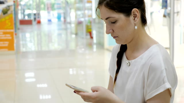 junge-Frau-sitzt-auf-einer-Bank-in-einem-Einkaufszentrum-mit-einem-Telefon
