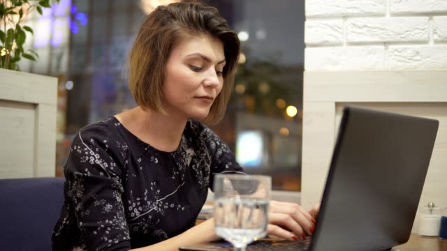 Junge-Geschäftsfrau,-die-sitzen-in-einem-Café-mit-einem-Laptop,-Arbeits--und-Trinkwasser