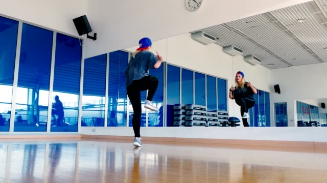Sporty-girl-in-cap-dancing-in-front-of-mirror-in-gym