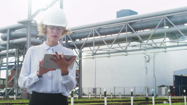 Woman-in-Hard-Hat-is-Walking-and-Using-Tablet-PC-in-Industrial-Environment