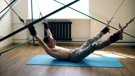 Junger-Mann-tun-Exircise-auf-Kasernierung-Yoga-Ausrüstung-und-ziehen-Sie-seine-Arme-und-Beine-mit-Seilen