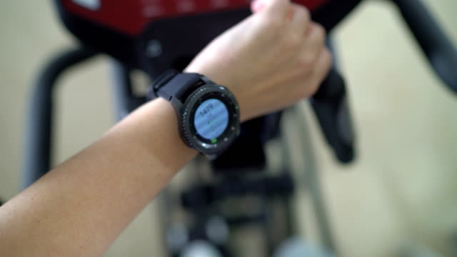 PoV-of-woman-doing-cardio-on-elliptical-trainer-checking-workout-on-smart-watch
