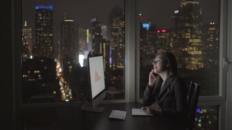 Mujer-atractiva-trabajar-con-una-computadora,-bolígrafo,-cojín-y-un-teléfono-en-el-edificio-de-oficinas-de-varios-pisos.-Llamar-a-colegas,-gran-ciudad-puede-verse-a-través-de-la-ventana.