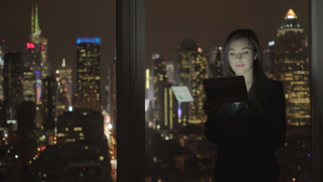 Attraktive-Brünette-nachts-im-Büro-arbeiten.-Geschäftsfrau-arbeiten-mit-digitalen-Tablet-mit-Stadtbild-Ansicht-im-Amt.