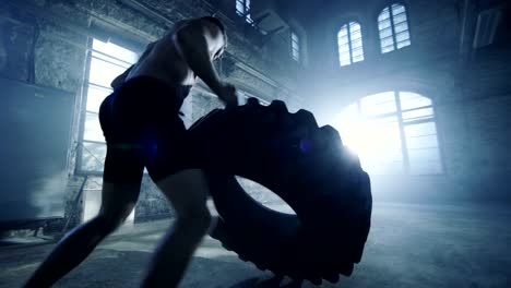 Strong-Muscular-Man-Lifts-Tire-as-Part-of-His-Fitness-Routine.-He's-Covered-in-Sweat-and-Works-out-in-a-Abandoned-Factory-Remodeled-into-Gym.