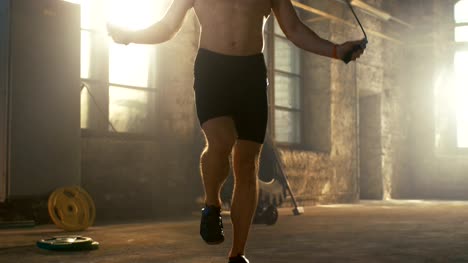 Athletic-Shirtless-Fit-Man-Exercises-with-Jump-/-Skipping-Rope-in-a-Deserted-Factory-Hardcore-Gym.-He's-Covered-in-Sweat-from-His-Intense-Fitness-Training.