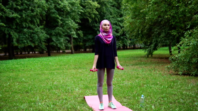 Joven-mujer-musulmana-vestida-con-una-burqa-haciendo-ejercicios-con-pesas-en-un-parque-de-verano