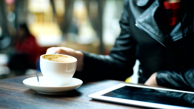 Woman-hand-puts-a-cup-of-coffee-near-the-tablet-in-cafe