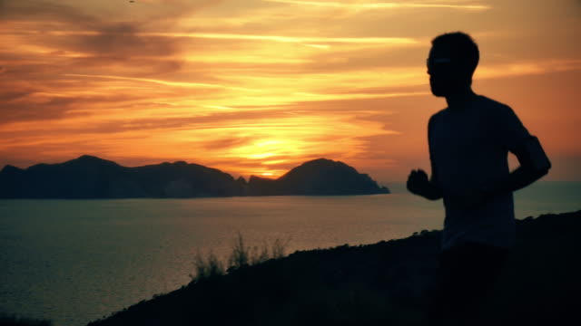Silhouette-eines-Mannes-auf-einem-Berg-auf-einer-Insel-bei-Sonnenuntergang-mit-dem-Meer-im-Hintergrund-laufen