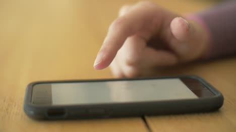 Closeup-del-dedo-de-la-mujer-pantalla-smartphone-en-mesa-de-desplazamiento