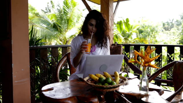 Chica-joven-Laptopn-ordenador-en-terraza-de-verano-durante-el-desayuno,-hermosa-WomanTypung-teclado-mientras-que-beber-jugo-de