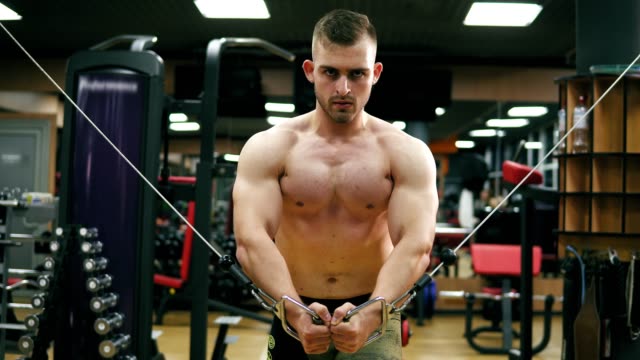 Closeup-view-of-a-shirtless-handsome-athletic-man-doing-pectorals-on-the-crossover-trainer-in-the-gym.-Shot-in-4k