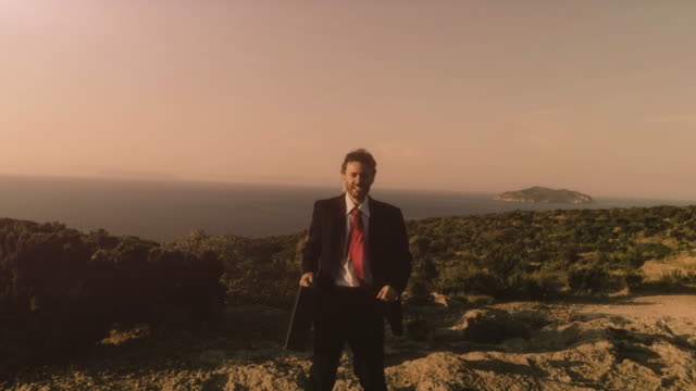 Man-in-elegant-suit-with-briefcase-running-on-top-of-a-cliff-on-an-island-and-exulting