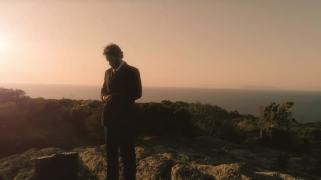 Man-in-elegant-suit-straightens-his-jacket-on-top-of-a-cliff-on-an-island