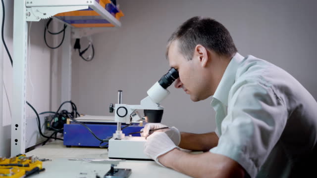Ingeniero-electrónico-es-mirar-en-un-microscopio-en-el-laboratorio-y-estudiar-mecanismo-pequeño,-tocar-detalles-por-pinzas