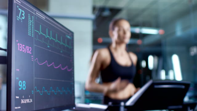 Medizinischer-Monitor-zeigt-EKG-Messwert-von-einer-Sportlerin-laufen-auf-einem-Laufband.-Monitor-im-Mittelpunkt.
