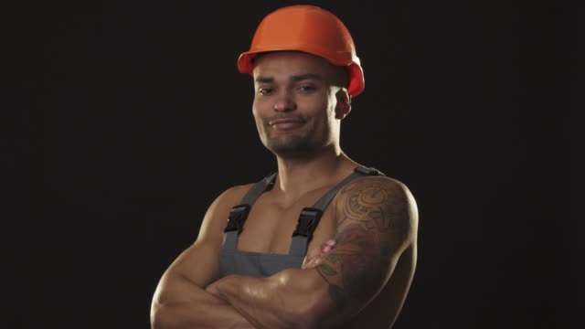 Glücklich-muskulösen-afrikanischen-männlichen-Baumeister-in-Bauarbeiterhelm-Lächeln-zeigt-Daumen-nach-oben