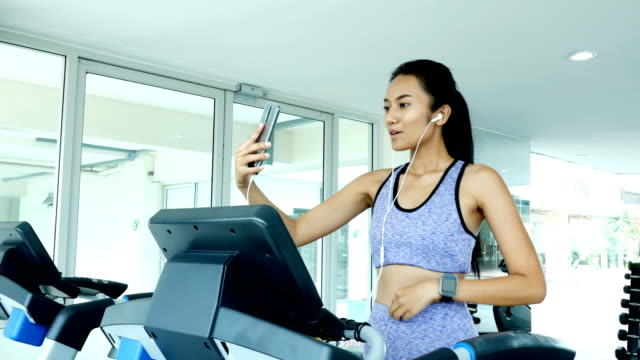 Frau-mit-Smartphone-während-der-Übung.-Asiatische-Frau-Übung-im-Fitnessstudio.-Sport-und-Reaktion-Konzept.-4k-Auflösung.