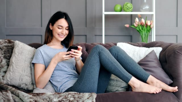 Young-pretty-woman-sitting-on-sofa-with-smartphone