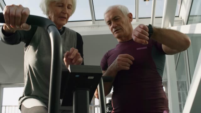 Entrenador-de-ancianos-ayudando-a-mujer-Senior-en-gimnasio