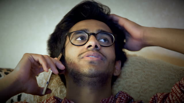 Primer-plano,-guapo-hombre-indio-en-gafas-hablando-por-teléfono,-sentado-en-el-sofá