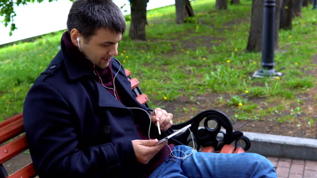 Un-hombre-escucha-música-y-trabaja-en-una-tablet-en-el-parque.