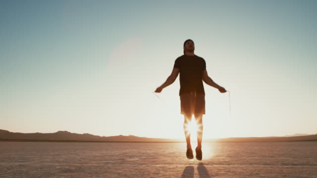 Slow-Motion-sportlicher-Mann-arbeiten,-draußen-in-der-Wüste-bei-Sonnenuntergang-Seilspringen