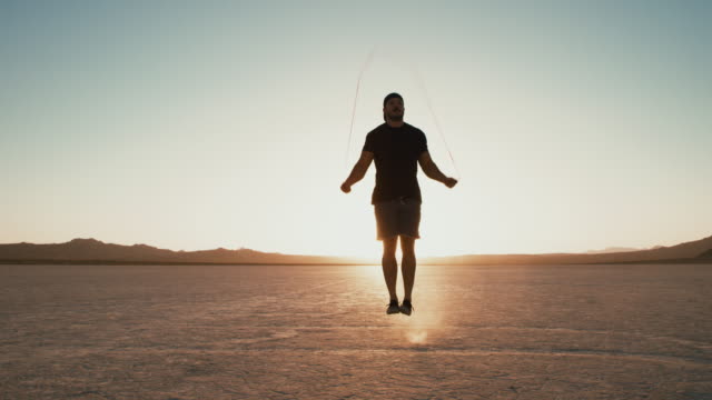 Slow-Motion-sportlicher-Mann-arbeiten,-draußen-in-der-Wüste-bei-Sonnenuntergang-Seilspringen