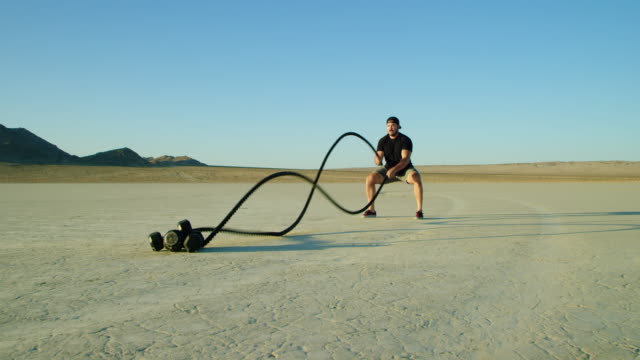 Deportiva-hombre-haciendo-ejercicios-de-cuerda-extrema-batalla-fuera-en-el-desierto