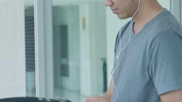Young-asian-man-running-on-the-treadmill-in-the-gym-with-earphones