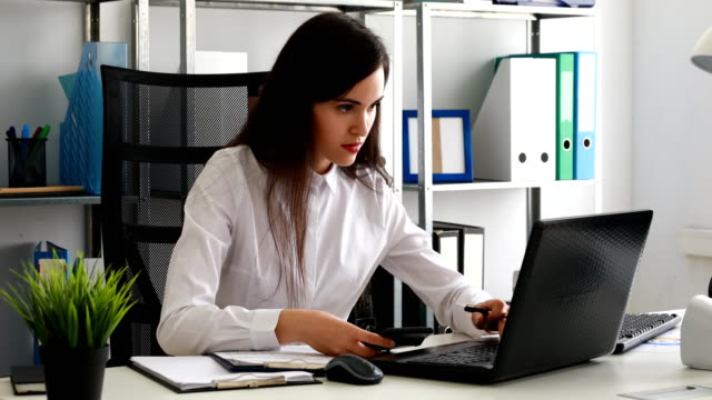 Geschäftsfrau,-am-Laptop-arbeiten-und-rechnen-mit-Taschenrechner-im-modernen-Büro