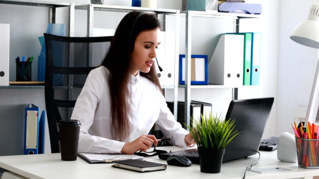 Frau-auf-Kopfhörer-sprechen-und-mit-Laptop-im-modernen-Büro