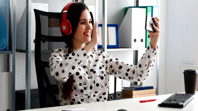 geschäftsfrau-in-rot-Kopfhörer-Videoaufnahmen-auf-Smartphone-im-modernen-Büro