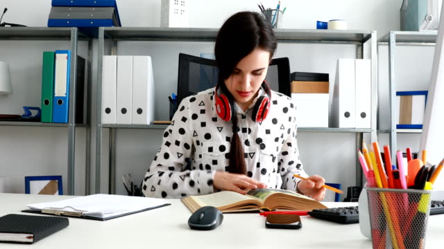 woman-with-red-headphones-on-shoulders-closing-book-and-leaning-back