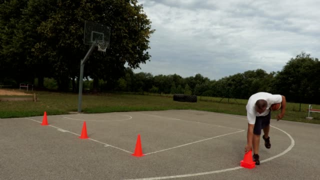 Athlet-sammelt-orange-Kegeln-aus-dem-Basketballplatz