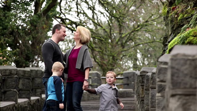 A-mom-and-dad-with-their-two-kids-walk-down-a-set-of-stairs-in-a-park-and-kiss