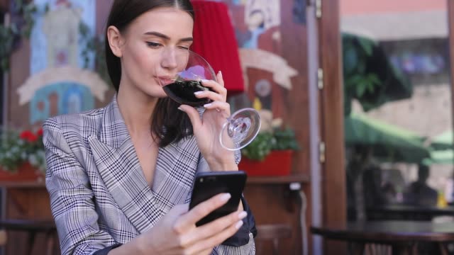 Smiling-Woman-Drinking-Wine-And-Using-Phone-At-Restaurant