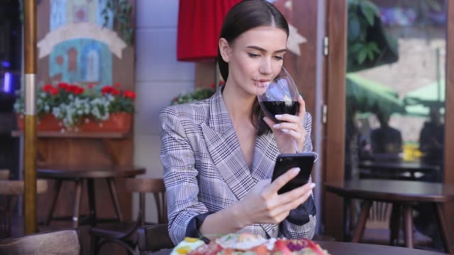 Mujer-sonriente-bebiendo-vino-y-usar-el-teléfono-en-el-restaurante