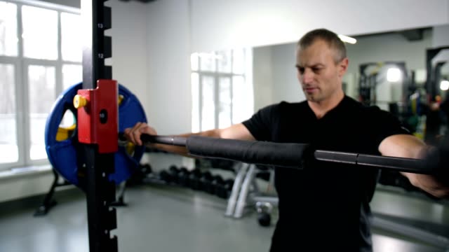 A-strong-man-fits-the-barbell,-takes-it-on-the-shoulders-and-does-squats-4K-Slow-Mo
