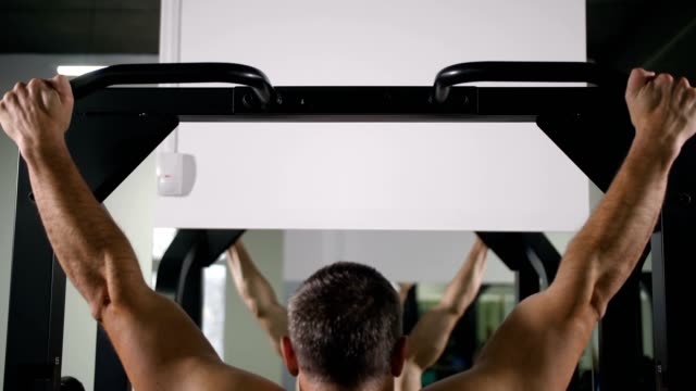 A-man-with-a-muscular-back-pulls-up-on-a-simulator-4K-Slow-Mo