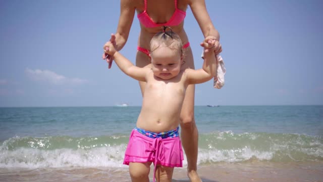 Mom-and-daughter-walk-along-the-seaside-along-the-sand-in-pink-swimsuits.-4K
