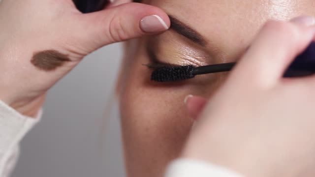 Master-is-using-black-mascara-on-womans-eyes,-performing-make-up