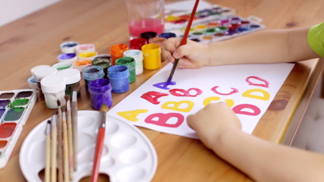 Kind-schreibt-Briefe-mit-einem-Pinsel-auf-einem-weißen-Blatt-Papier