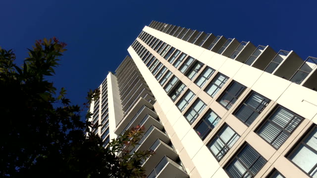 Motion-of-high-rise-building-and-blowing-tree-leaf-against-blue-sky