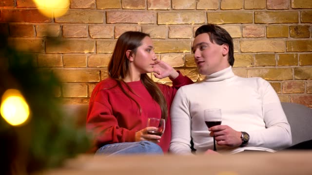 Porträt-des-kaukasischen-Brautpaar-auf-Sofa-sitzen-und-trinken-Wein,-die-in-gemütlicher-Atmosphäre-miteinander-reden.